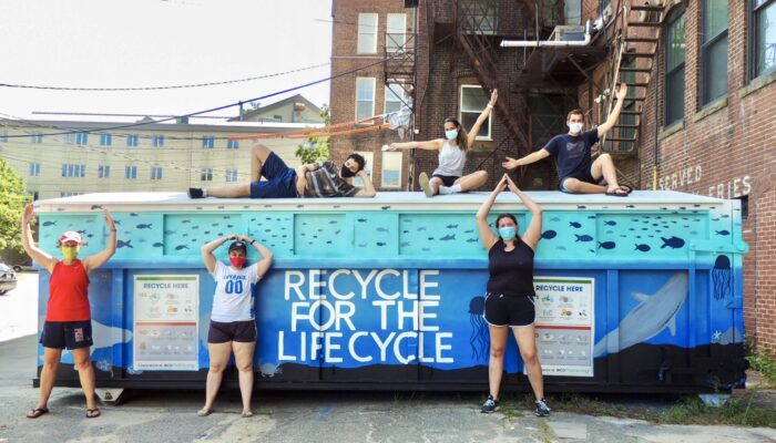 UMAA A group of people pose on top of and beside an ecomaine Silver Bullet, painted by a local artist, that reads Recycle for the Lifecycle