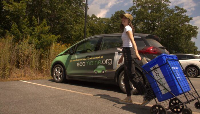 Zoe Malia wheels a recycling bin towards an Ecomaine EV in a parking lot