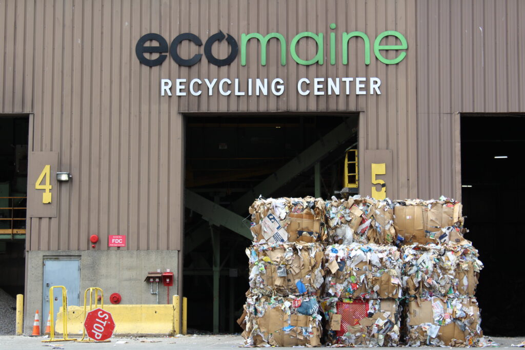 The front entrance of ecomaine's recycling center showing two open garage bays and a multiple stacked paper bales